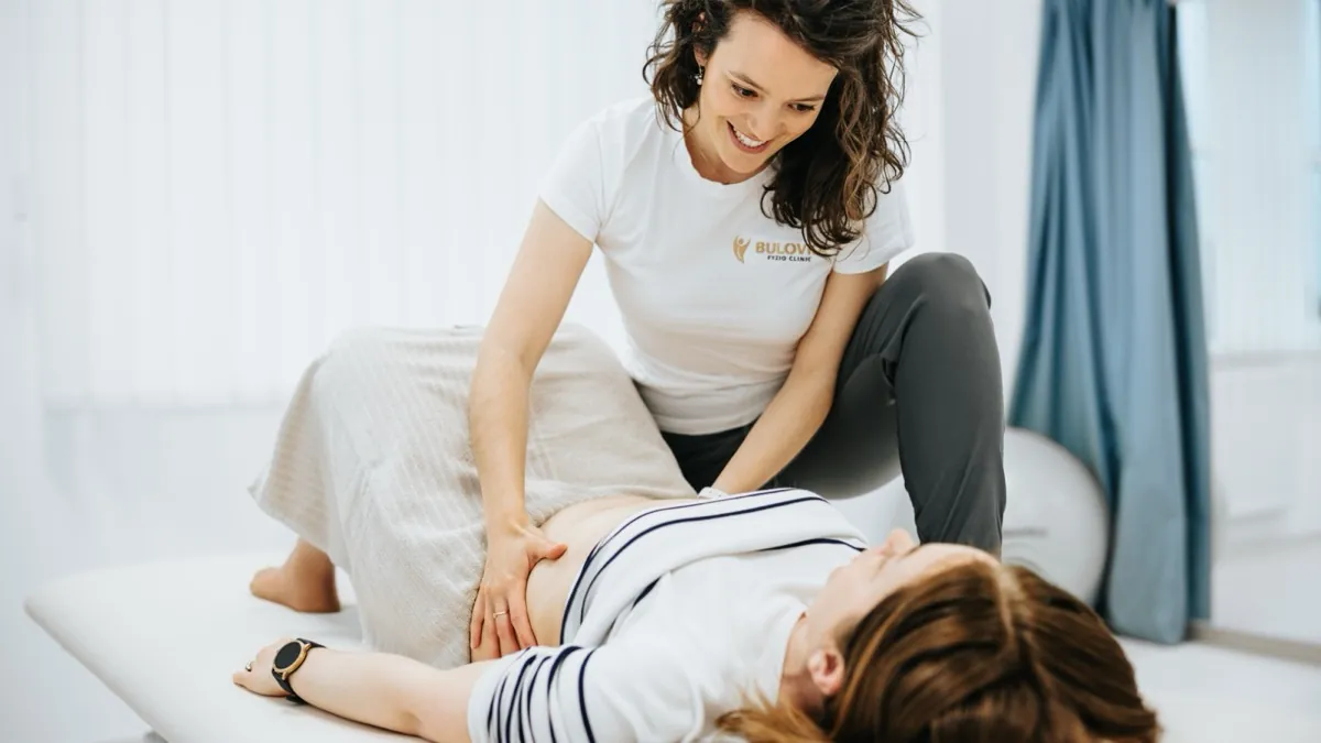 Chuyên viên vật lý trị liệu mỉm cười khi trị liệu vùng bụng và khung chậu cho khách hàng